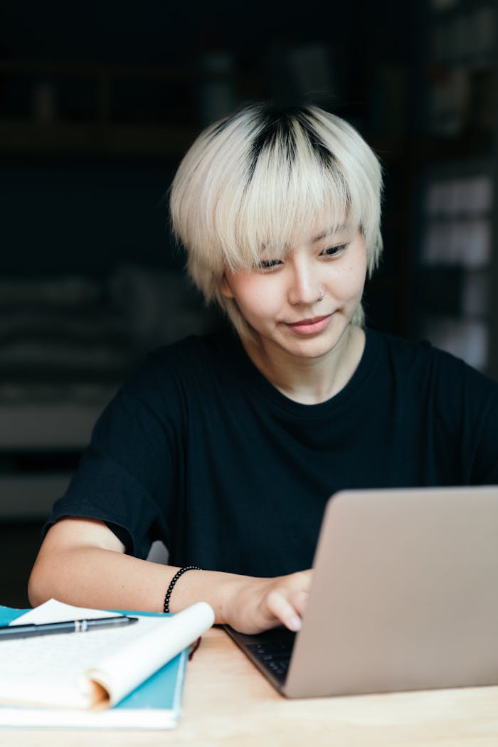 Cheerful young Asian woman browsing laptop indoors, studying or freelancing in a casual setting.